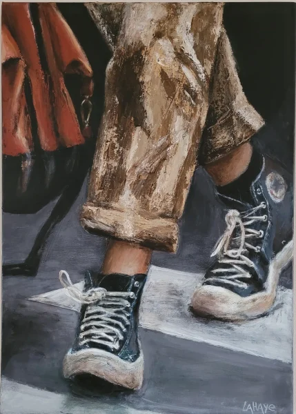Deux paires de Converse noires traversant un passage piéton, pantalon beige retroussé, un manteau rouge en arrière-plan.